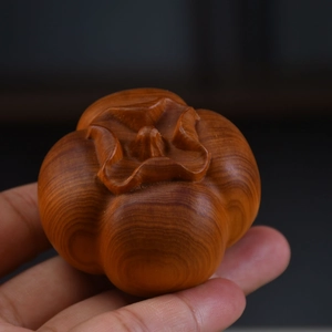 Macro shot of hand holding a carved red sandalwood persimmon pendant for good luck
