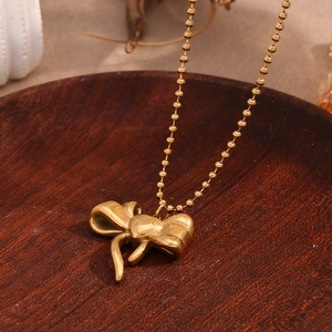 Detail of 18K gold-plated 3D bow pendant with delicate bead chain on dark wood background