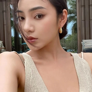 Close-up of golden textured teardrop earrings worn by a model in a natural setting