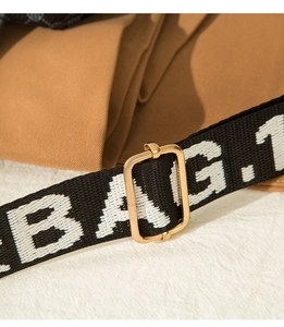 Detail of black woven shoulder strap with white text and polished gold metal buckle