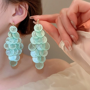 Close-up of mint green shell-textured layered circular drop earrings worn by a model