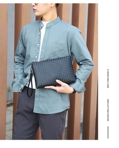 Man holding a black woven leather clutch bag with wrist strap in a stylish business setting