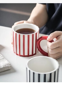 Close-up of ceramic mugs with red and black vertical stripes in a cozy home setting