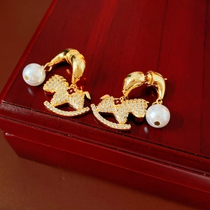 Macro shot of gold-plated rocking horse pearl earrings with pavé crystals on a wooden box