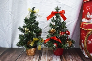 Mini Christmas trees with gold and red ribbons in woven baskets on wooden surface