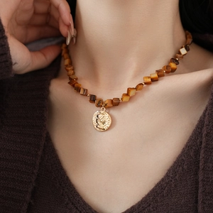Close-up of a vintage brown beaded necklace with a golden circular portrait coin pendant