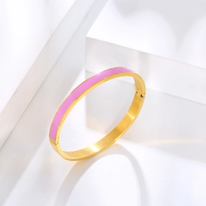 Close-up of a gold stainless steel bangle with pink enamel on white geometric blocks