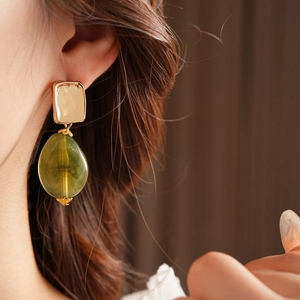 Close-up of vintage drop earring with gold square stud and green resin teardrop pendant