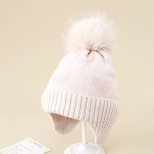 Detailed knit texture of girls winter hat with pink heart jacquard and faux fur pompom