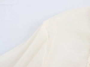 Close-up detail of cream cotton linen fabric texture and delicate lace stitching on sleeve