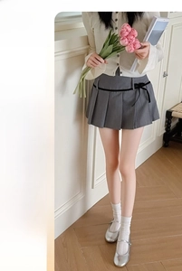 Detail of grey pleated skirt featuring a black belt and decorative bow in school style