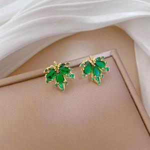 Detail view of golden maple leaf stud earrings with green crystals on white silk