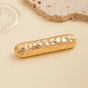 Detailed close-up of golden hair tie with hammered metal texture and minimalist design