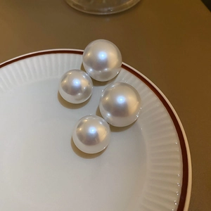 Close-up of four round white pearls in various sizes on a white ceramic plate