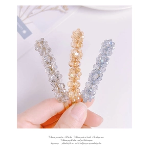 Detail of three beaded crystal flower hair clips in champagne, grey, and blue colors