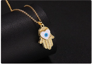 Macro shot of gold Hamsa hand pendant with blue evil eye heart and zircon inlay