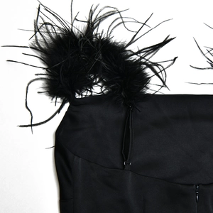 Gros plan d'une robe en satin noir avec bordure en plumes et fermeture éclair invisible