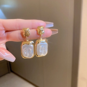 Close-up of vintage gold earrings with pleated metal texture and pearl-like square pendant