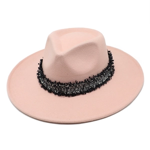 Détail d'un chapeau fedora en laine rose avec un ruban décoratif tissé à glands noirs