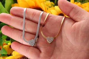 Macro detail of snake chain necklace with sparkling zircon heart pendant in hand