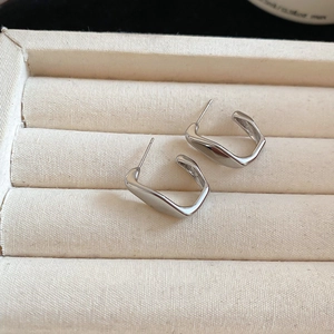 Macro shot of silver C-shaped irregular geometric earrings on a beige textured jewelry box