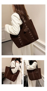 Detail of dark brown suede tote bag with silver studs and heart-shaped charm on a model