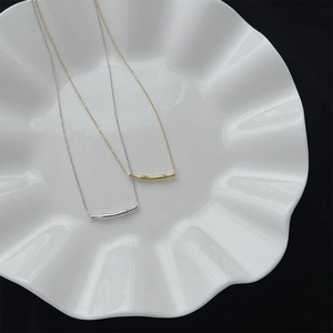 Colliers à pendentifs bambou or et argent sur plateau blanc avec fond noir profond