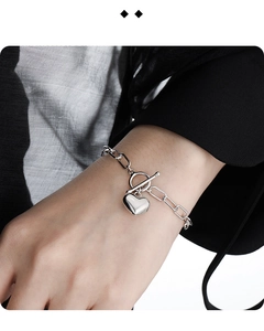 Macro close-up of a silver heart charm bracelet with OT toggle clasp on a wrist