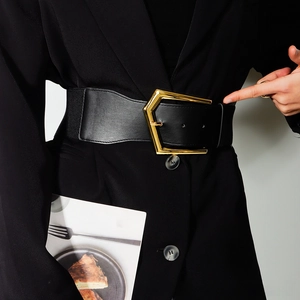 Detail of black wide elastic belt with polished gold pentagonal buckle on waist