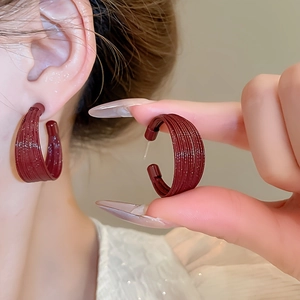 Close-up of deep red C-shaped hoop earrings with a detailed brushed metal texture finish