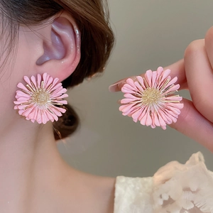 Detailed view of handmade pink raffia daisy earrings with gold stamen accents on model