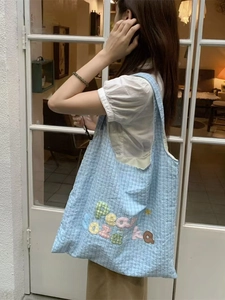 Blue plaid tote bag with rainbow embroidery shown on a model in a bright setting