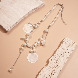 Elegant pearl and shell tassel necklace with silver accents on a minimalist stone background