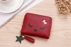 Detail of red cartoon wallet featuring eyelash pattern, pink bow, and leather tassel