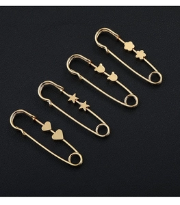 Detail of four golden metal safety pins with heart, star, bear and flower charms
