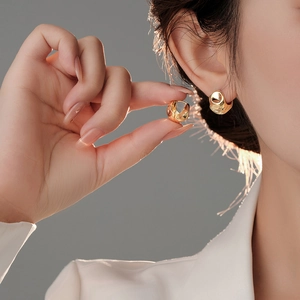 Close-up of model wearing irregular gold hoop earrings with a polished glossy finish