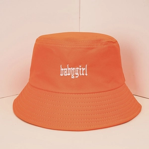 Dettaglio del ricamo babygirl bianco su tessuto di cotone arancione del cappello a secchiello