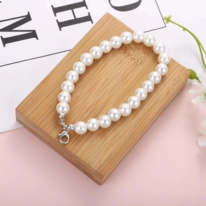 Elegant white faux pearl chain with silver lobster clasp on a minimalist wooden block