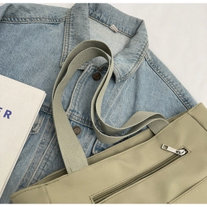 Close-up of khaki nylon tote bag with zipper pocket, styled with denim and a magazine