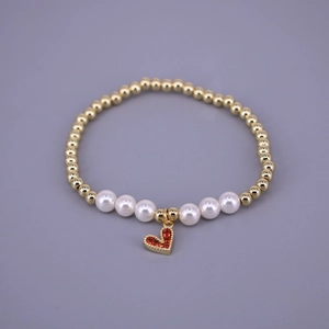 Detailed macro view of golden beads bracelet with white pearls and red heart charm