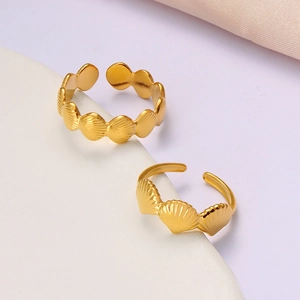Detail showing two gold shell textured open rings on white stone and fabric