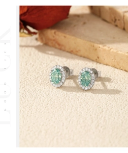 Close-up of silver earrings with oval green gemstones and small white crystal halo