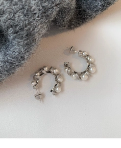 Macro shot of silver C-shaped earrings with white pearls and sparkling zircon details