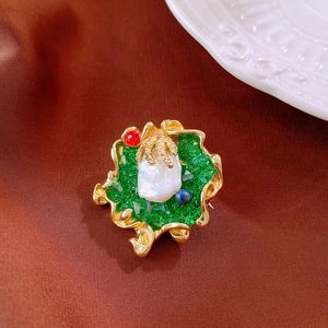 Close-up of vintage baroque pearl brooch with green stones on dark fabric