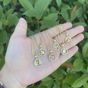 Hand holding six 18K gold zodiac necklaces with round micro-pave diamond pendants