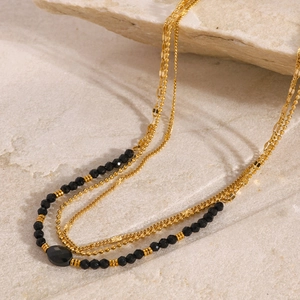 Three-layer gold necklace with black faceted beads and oval stone on natural rock background