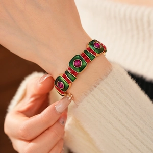 Detail of vintage gold bracelet featuring green enamel squares and red gemstone accents