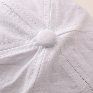 Close-up of the white cotton baseball cap showing top button and precise stitching detail