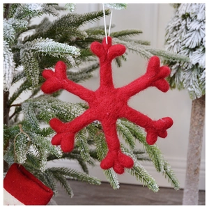 Detail of red wool felt snowflake ornament hanging on a snowy Christmas tree branch