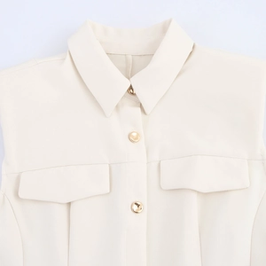 Detail of cream sleeveless dress with lapel collar, gold buttons, and chest pockets